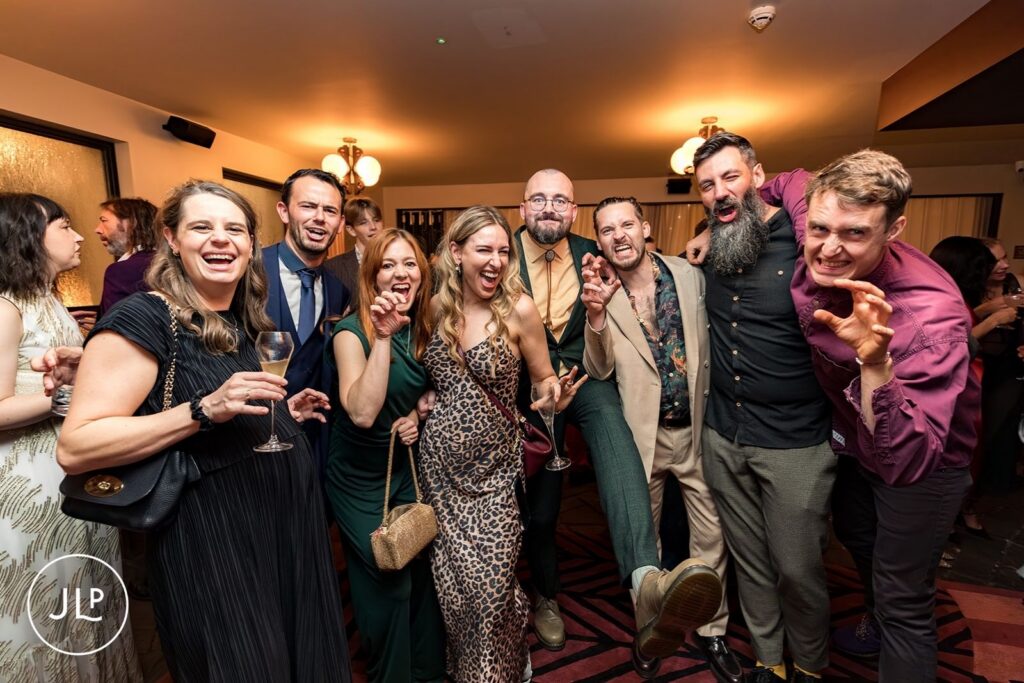 A group of wedding guests laughing and posing playfully with "claw" hands at a wedding reception at The Hoxton Holborn.