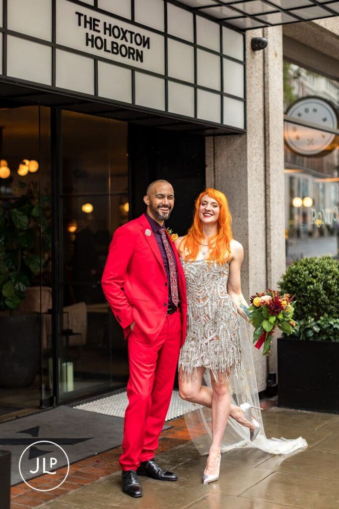 The newlyweds smile together under the marquee at the entrance of The Hoxton Holborn wedding venue in London.