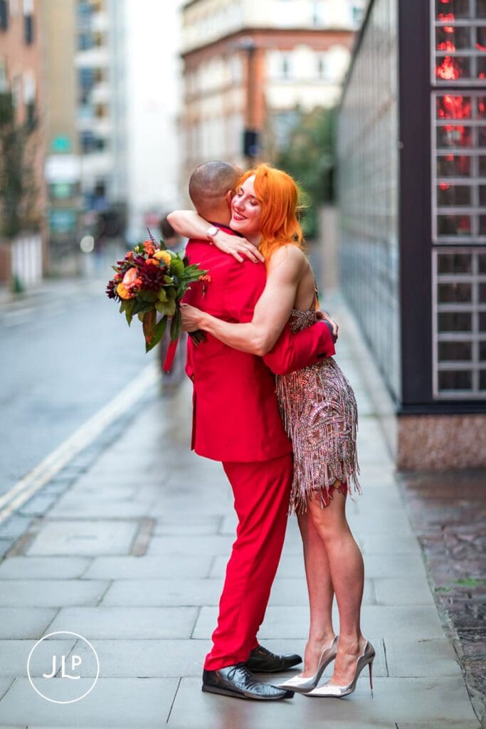 A romantic moment of a bride and groom hugging on a wet pavement during their urban London wedding.