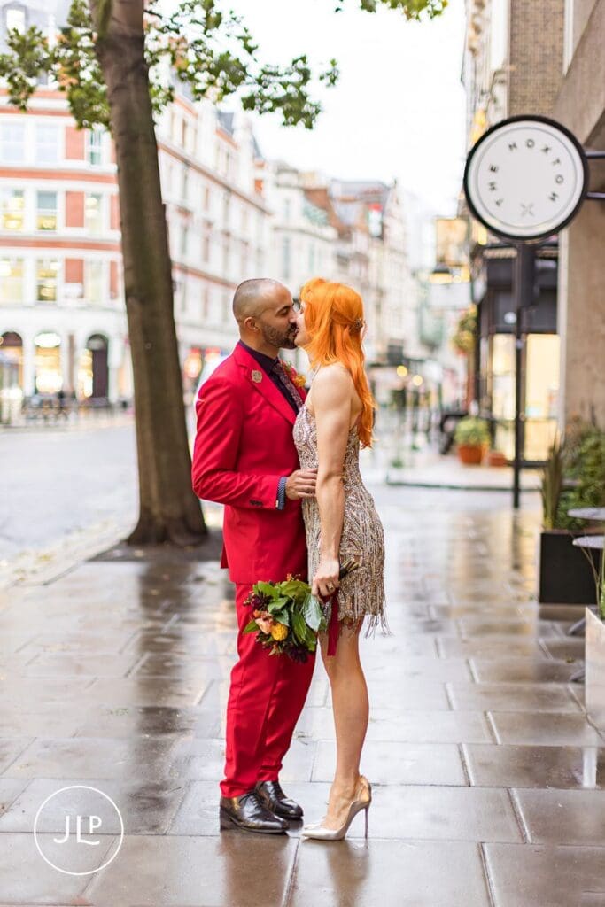The bride and groom share a kiss on the sidewalk outside their wedding venue at The Hoxton Holborn.