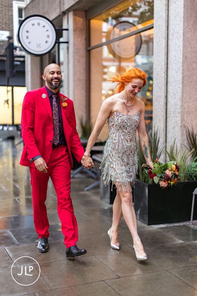 A happy couple holding hands and walking down a London street after their alternative wedding ceremony.