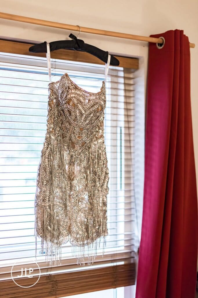 A short beaded wedding dress hangs by a window during bridal prep in London.