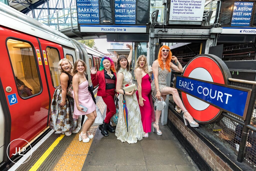 The bridal party cheers together at the Earl's Court station platform during a London wedding.