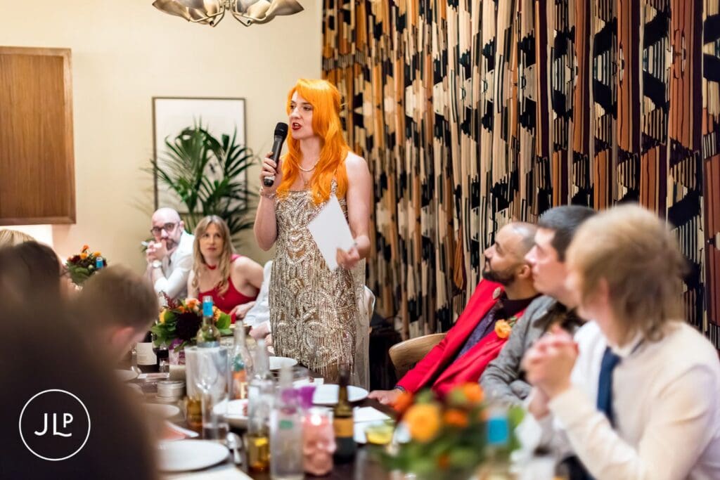 The bride with orange hair speaking into a microphone while holding a speech at her wedding reception dinner.