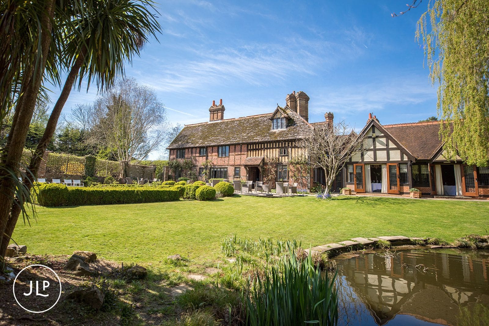 Back garden view of Langshott Manor, a romantic Surrey wedding venue with a pond and lawns.