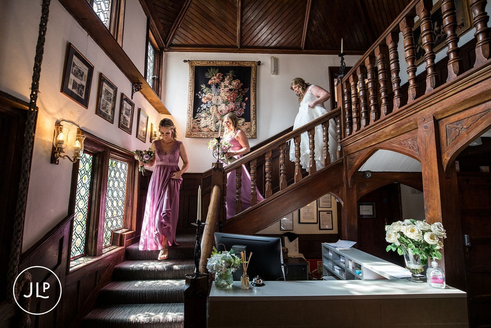Bride walking down the grand wooden staircase, captured by a Langshott Manor wedding photographer.
