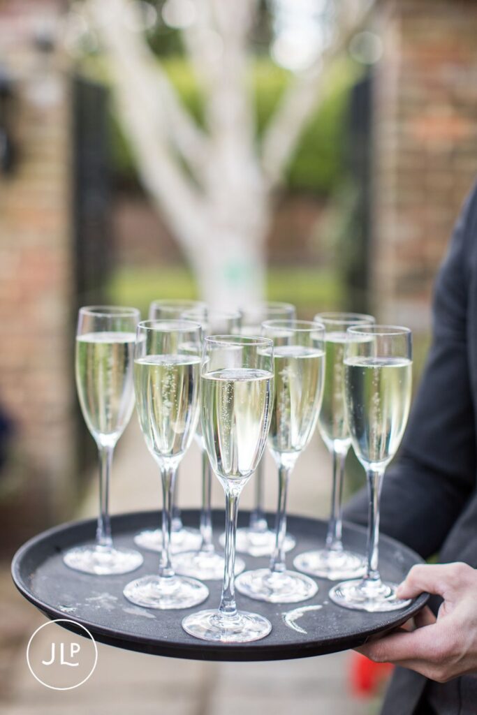 A tray of chilled champagne flutes being served to guests during a summer wedding reception in Surrey.