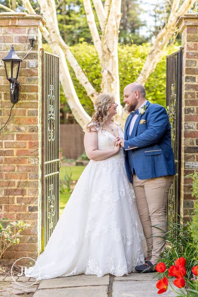 Bride and groom sharing a moment by the garden gates at Langshott Manor, a luxury Surrey wedding venue.