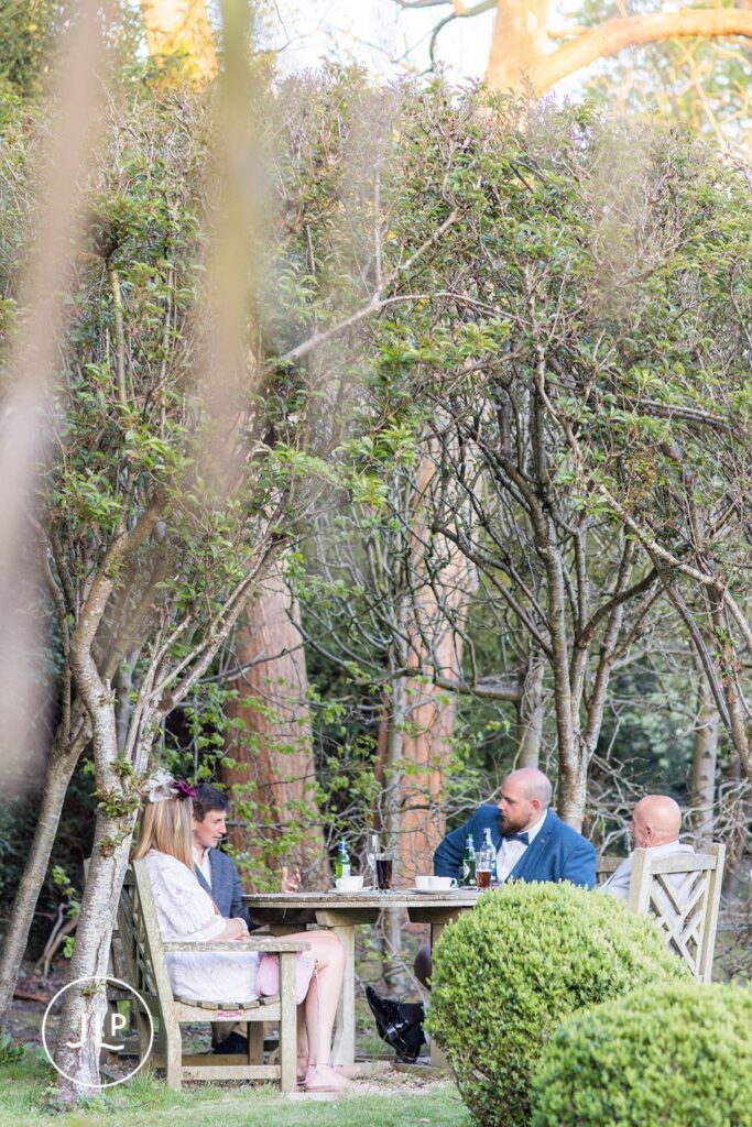 Wedding guests relaxing and chatting at an outdoor table in the historic gardens of Langshott Manor.