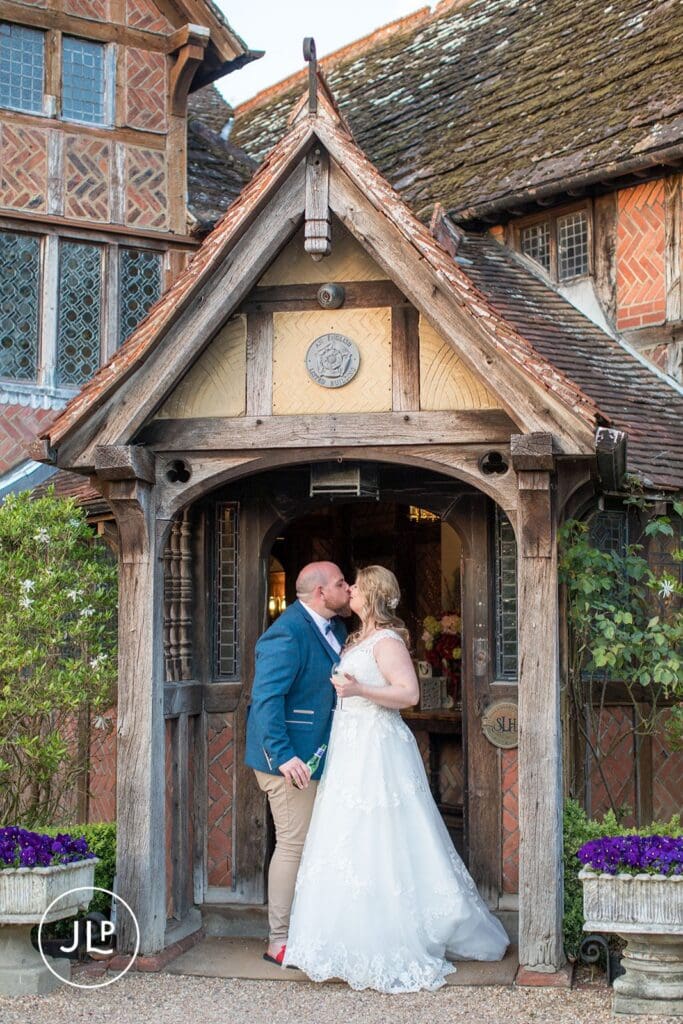 Romantic kiss at the historic timber-framed entrance of Langshott Manor, captured by a Surrey wedding photographer.