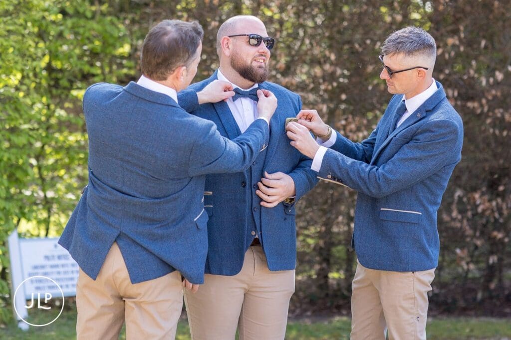 Groomsmen helping the groom with his bow tie at Langshott Manor, a luxury Surrey wedding venue.