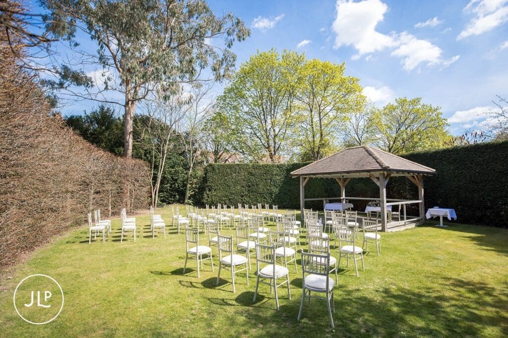 Outdoor wedding ceremony setup with white chairs and a wooden gazebo at Langshott Manor in Surrey.