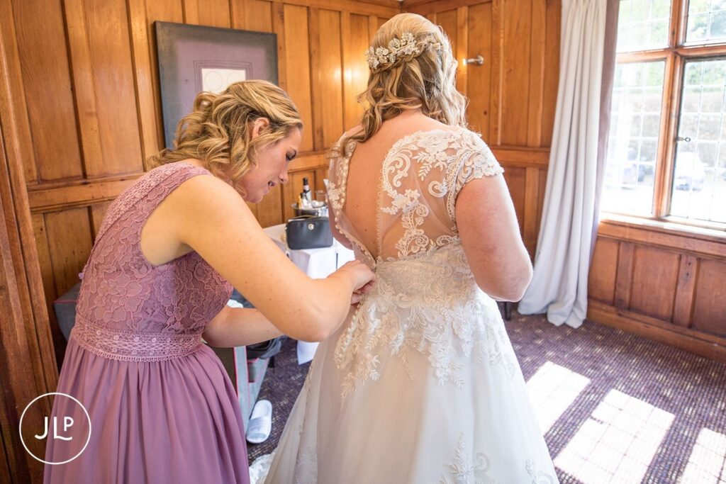 Langshott Manor wedding photography of the bridesmaid helping the bride into her lace wedding gown.