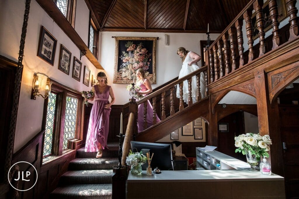 Bride and bridesmaids descending the historic wooden staircase at Langshott Manor boutique wedding venue.