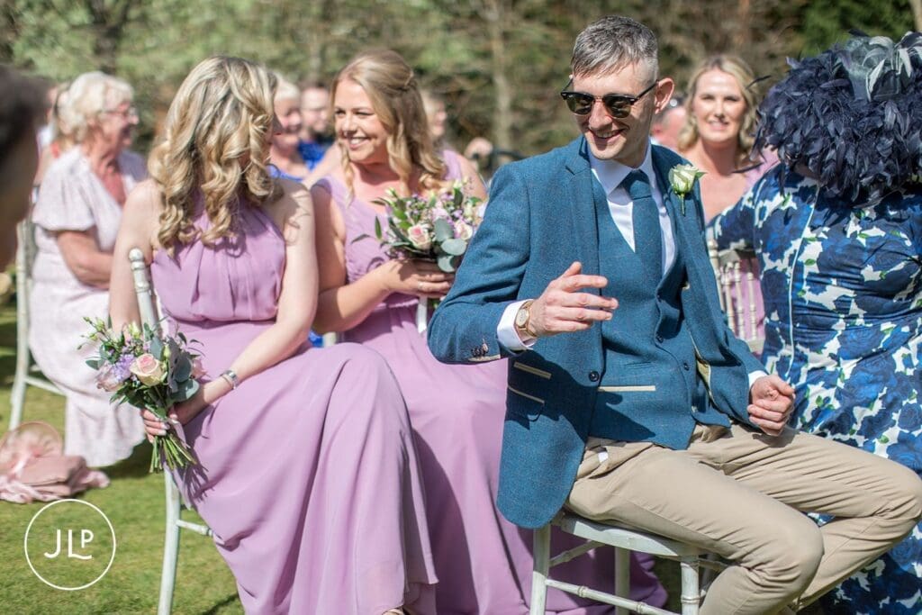 Candid wedding photography Surrey of a groomsman laughing during the outdoor ceremony at Langshott Manor.