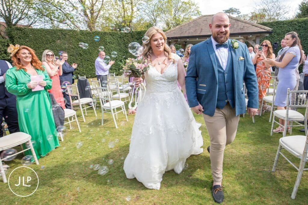 Newlyweds walking through bubbles at Langshott Manor, an award-winning Surrey wedding venue.