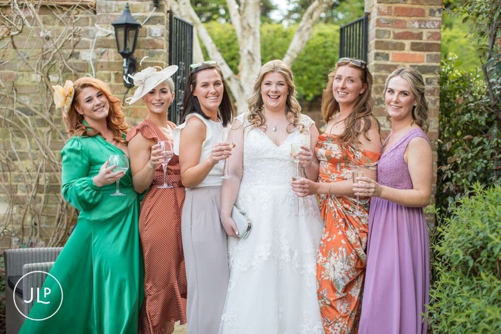 Bride posing with her bridesmaids enjoying drinks in the gardens of Langshott Manor wedding venue Surrey.