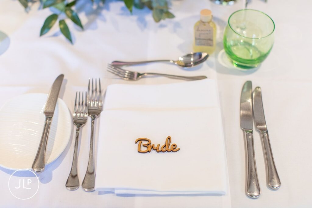 Elegant wedding table place setting for the bride with a custom wooden name tag and a small bottle of personalized favor.