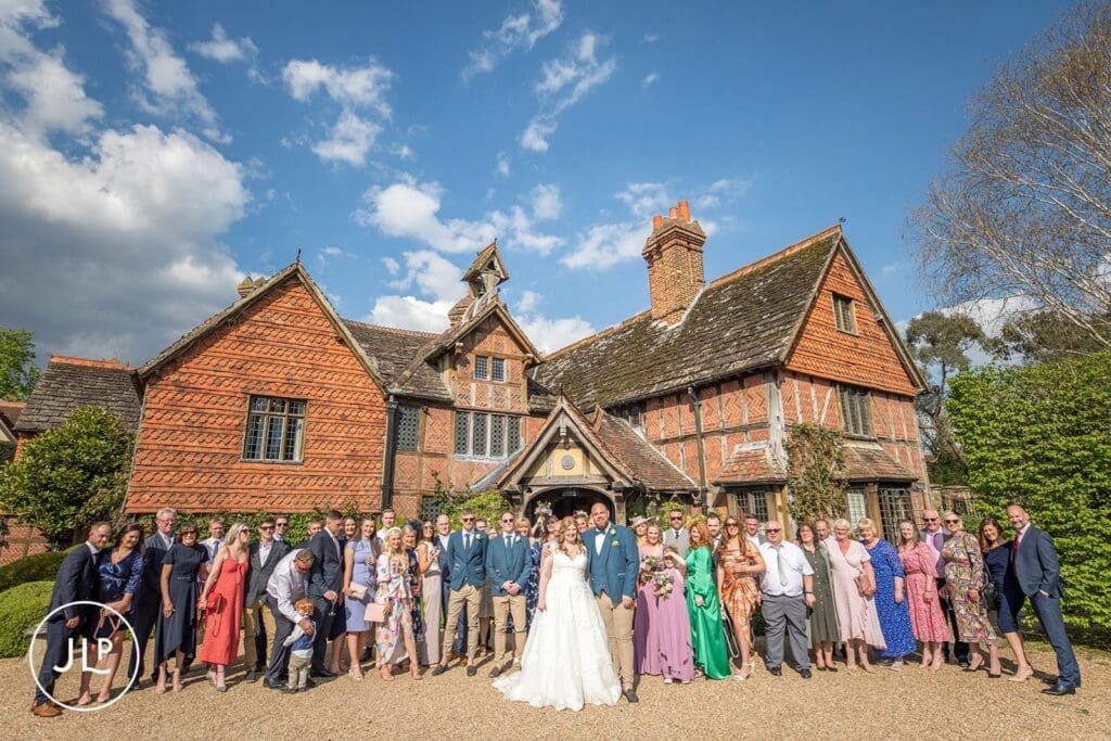 Large group wedding photo of the bride, groom, and guests in front of the historic Langshott Manor in Surrey.