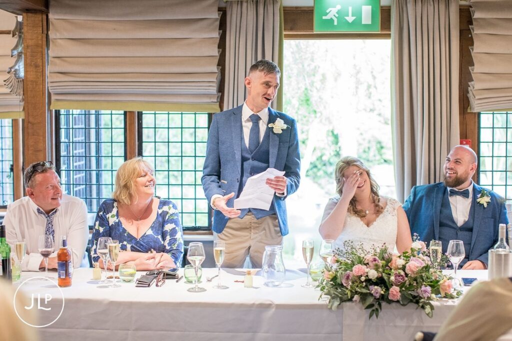 Best man giving a funny speech at the top table during a luxury Surrey wedding reception at Langshott Manor.