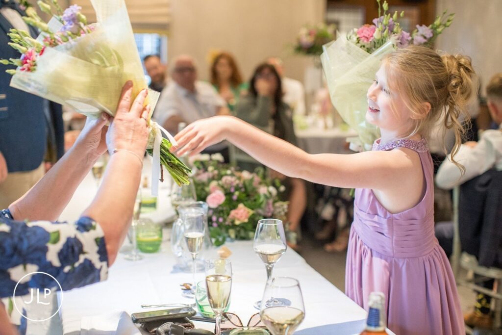 A young bridesmaid receiving a bouquet of flowers as a thank-you gift during wedding speeches in Surrey.
