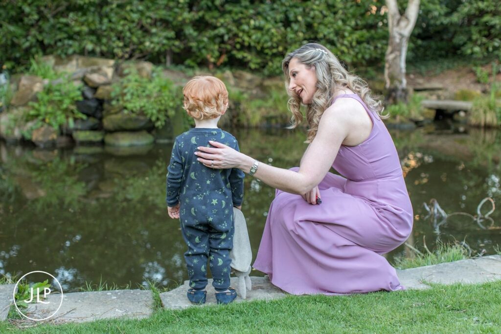 A wedding guest in a lavender dress showing a toddler the duck pond during a Surrey country house wedding.