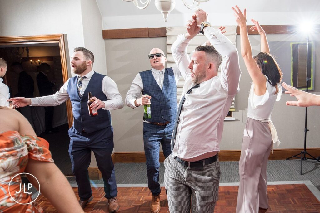 Male wedding guests enjoying the party and dancing at a wedding reception at Langshott Manor in Surrey.