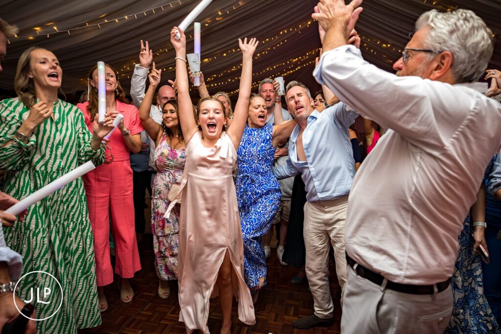 Guests dancing with foam glow sticks at a fun summer outdoor Surrey wedding reception at Painshill Park.