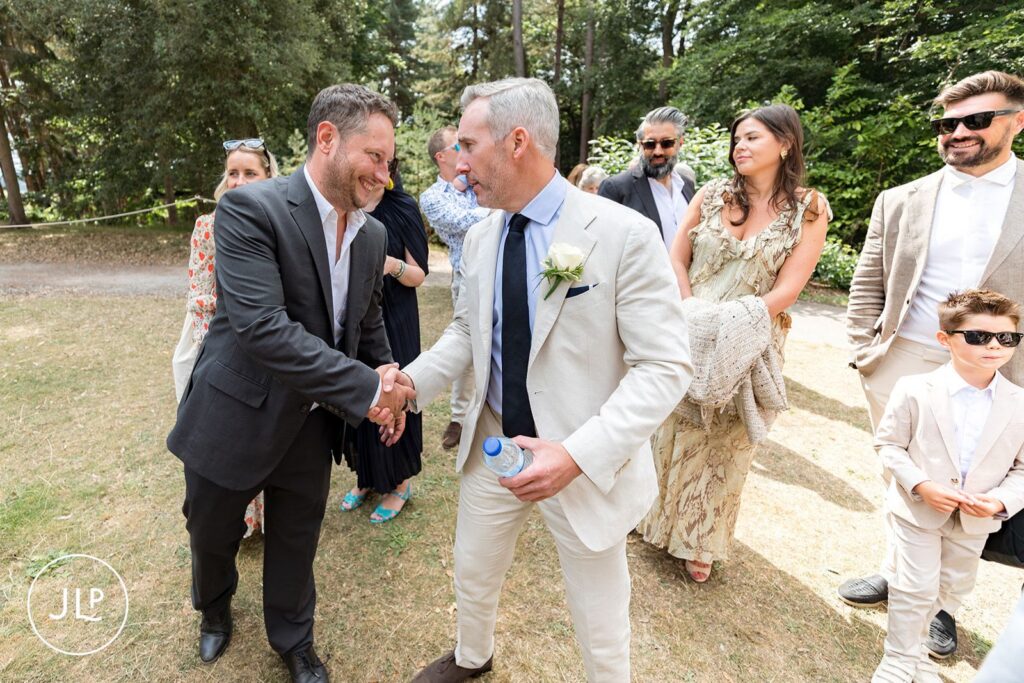 Groom shaking hands with a guest during an outdoor Surrey wedding at Painshill Park.