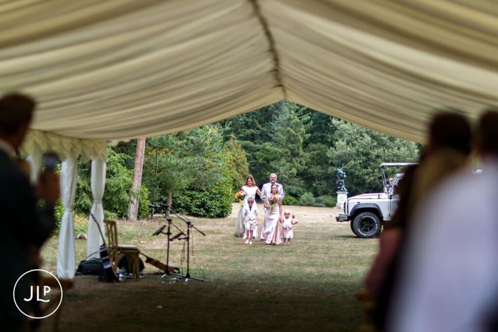 Natural wedding photography of a bridal procession walking toward a marquee at Painshill Park.