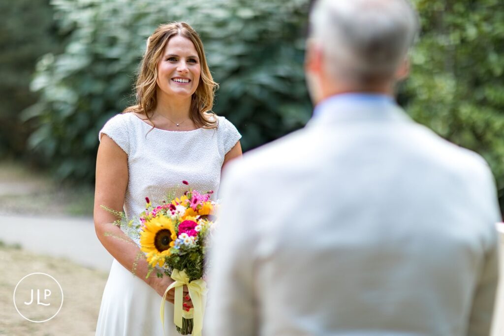 Smiling bride holding a sunflower bouquet, by an expert Painshill Park wedding photographer.