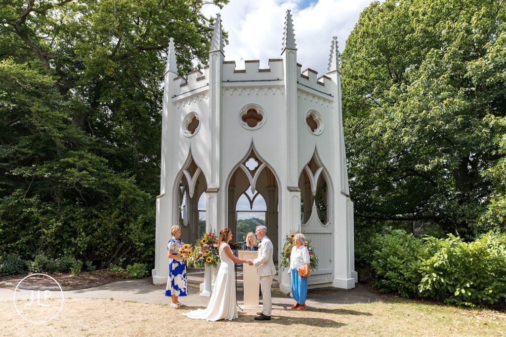 An outdoor wedding ceremony taking place at the Gothic Temple in Painshill Park Cobham.