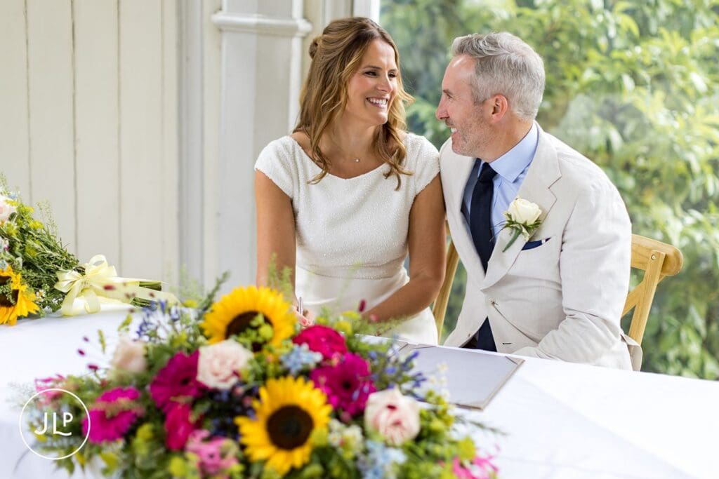 Bride and groom sign register at an outdoor Surrey wedding, captured by a Painshill Park wedding photographer.