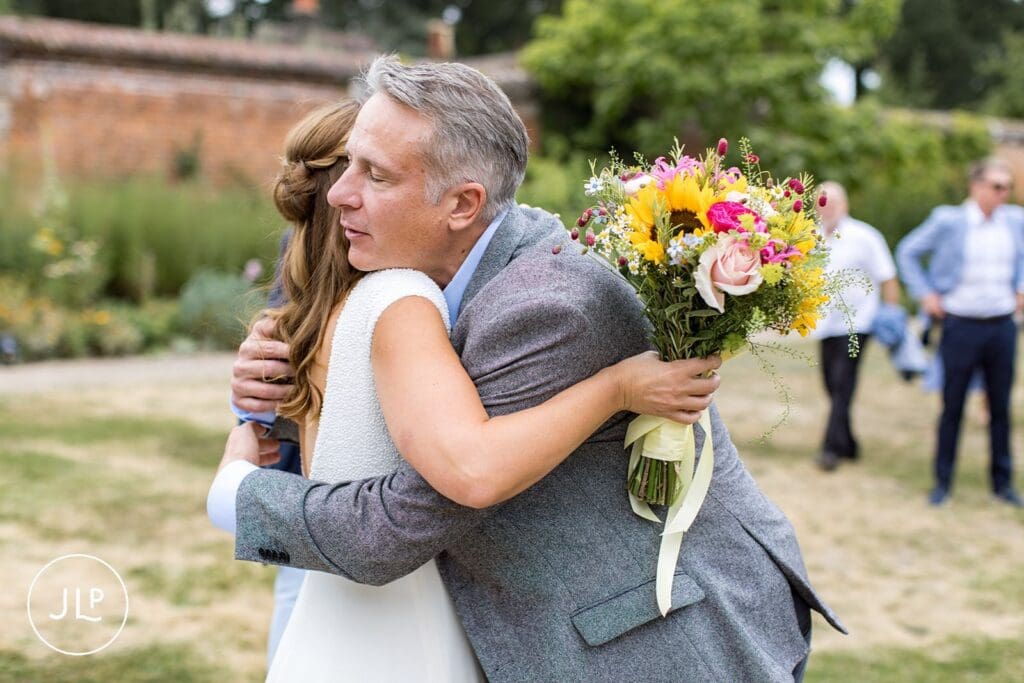 Candid wedding photography of a bride hugging a guest in the Walled Garden at Painshill Park.