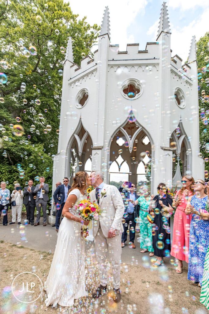 Bubble exit at a Painshill Park wedding, featuring candid wedding photography of newlyweds kissing.