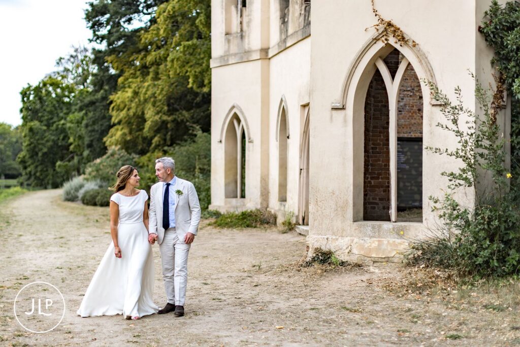 Natural wedding photography of a bride and groom walking outside the Ruined Abbey at Painshill Park Cobham.