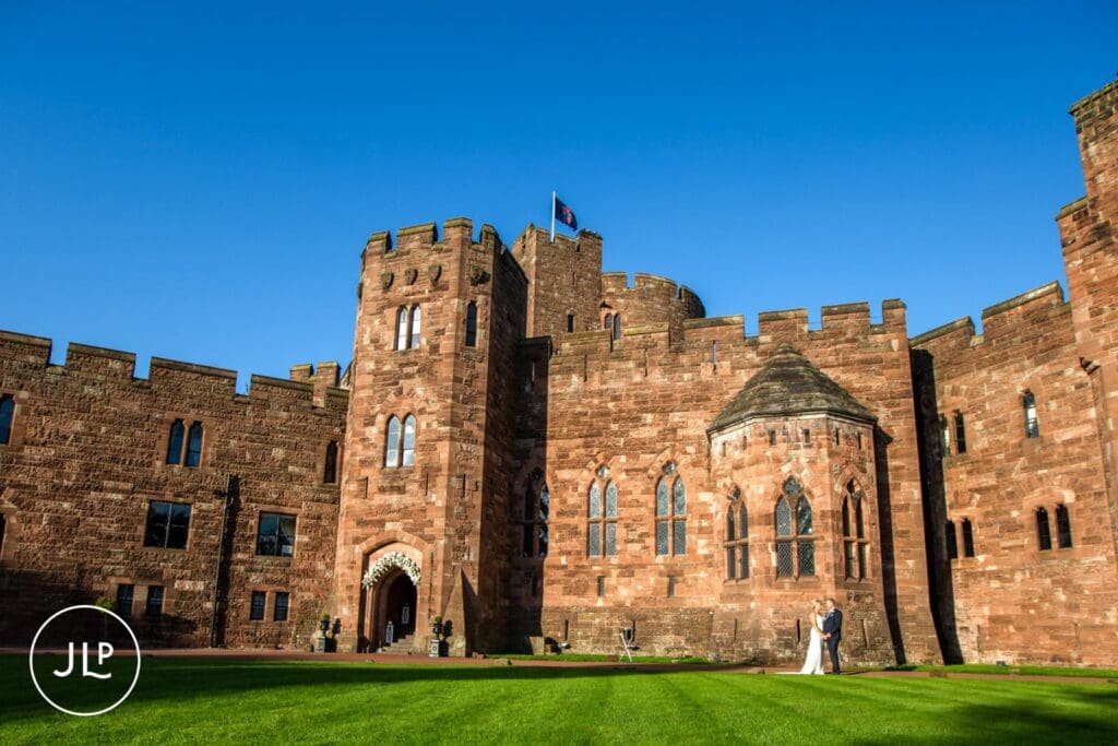 Wide portrait of a couple outside the historic luxury castle wedding venue at Peckforton Castle.