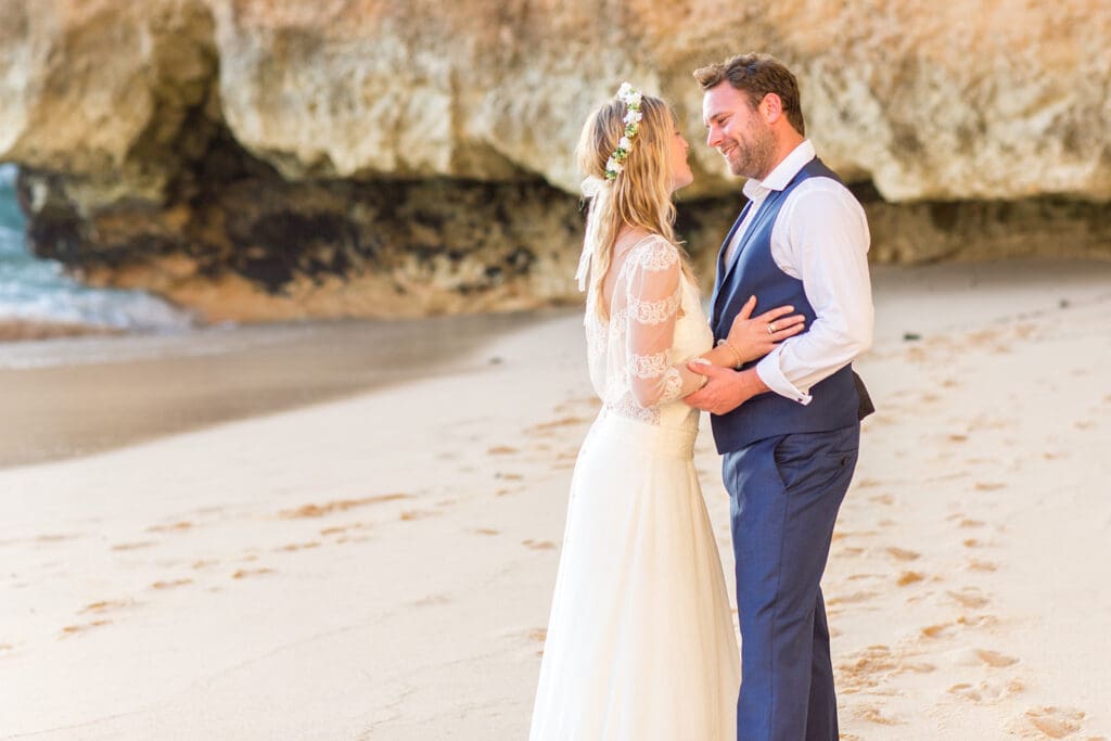 A romantic newlywed embrace during an Algarve beach wedding photoshoot against dramatic coastal cliffs.