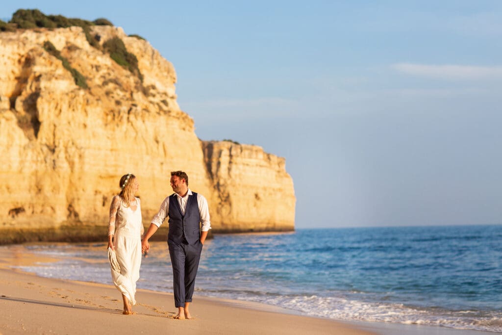 Newlyweds walking on a golden beach, captured by an Algarve beach wedding photographer in Portugal.