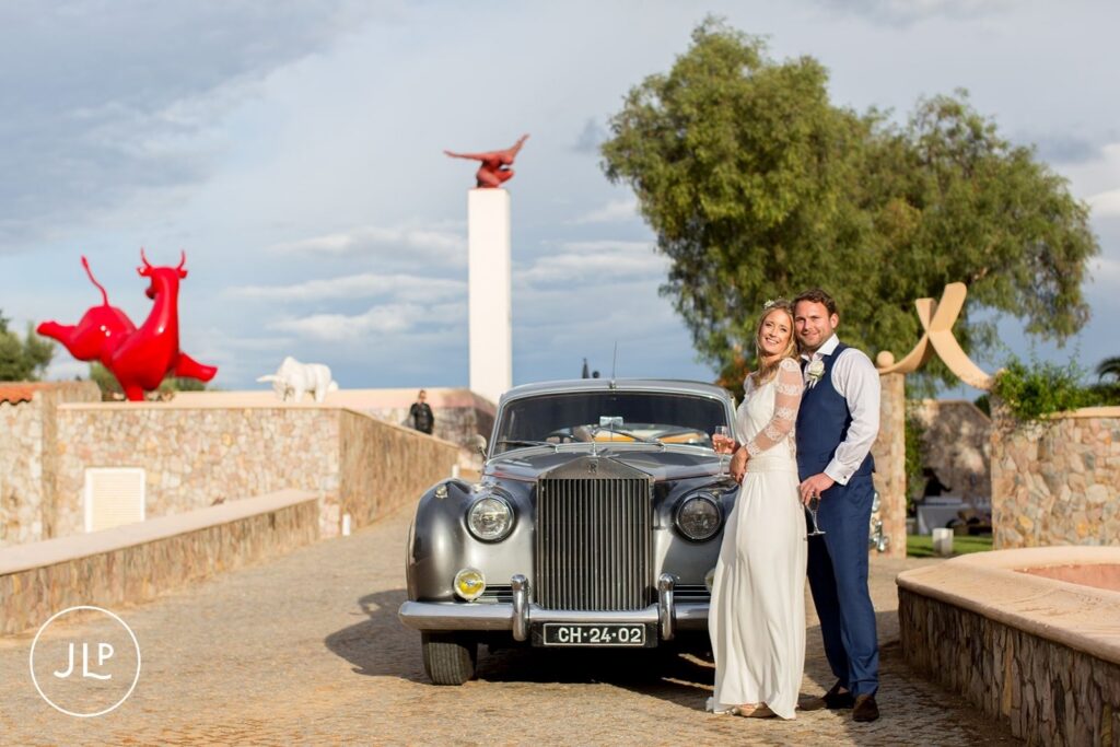 Ali and Matty posing with a vintage Rolls Royce at their Quinta dos Vales wedding at sunset.