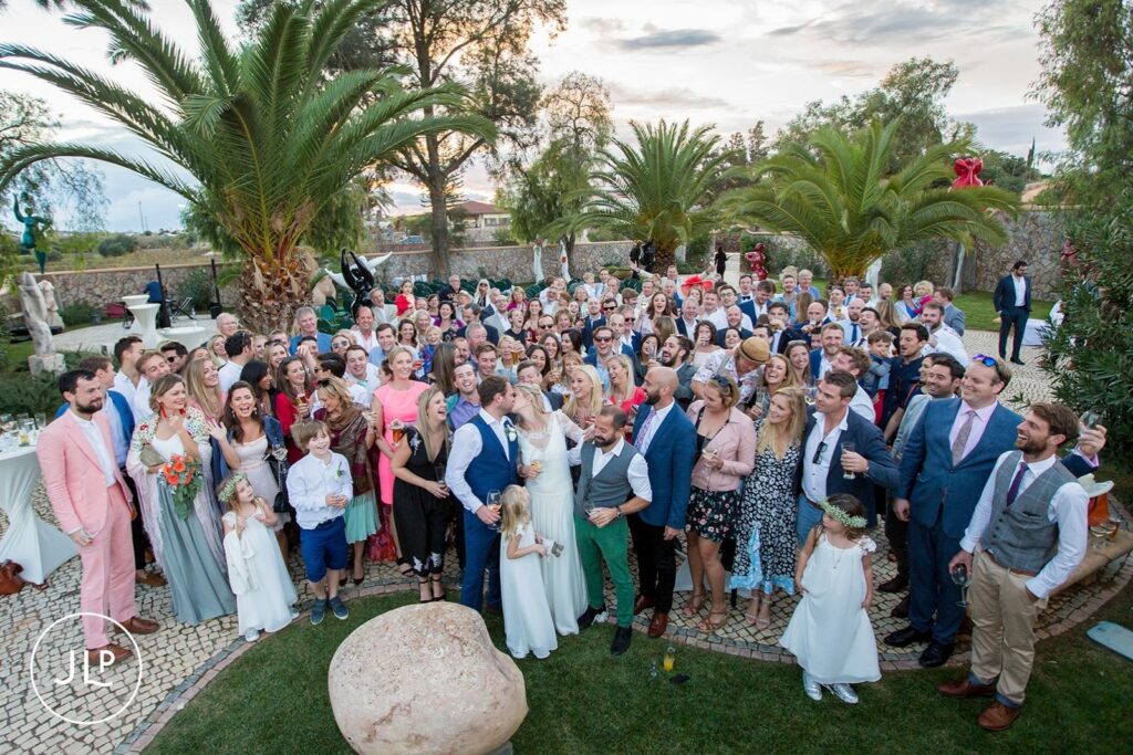 Aerial group shot of Ali, Matty, and guests under palm trees at a luxury Quinta dos Vales wedding in Portugal.