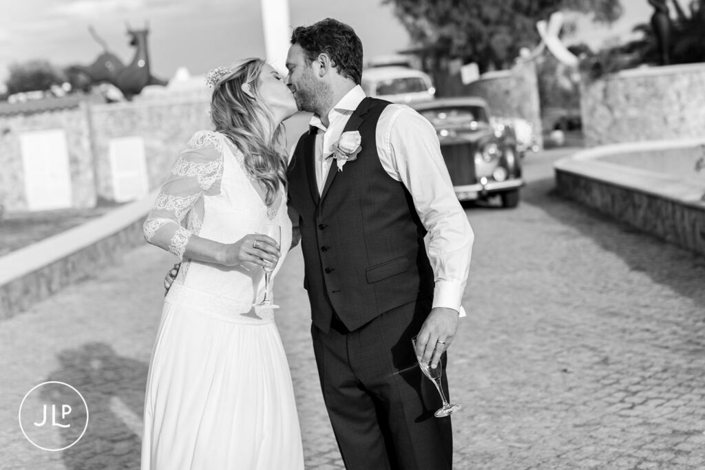 Romantic B&W kiss of Ali and Matty by their wedding car, shot by an Algarve luxury wedding photographer.