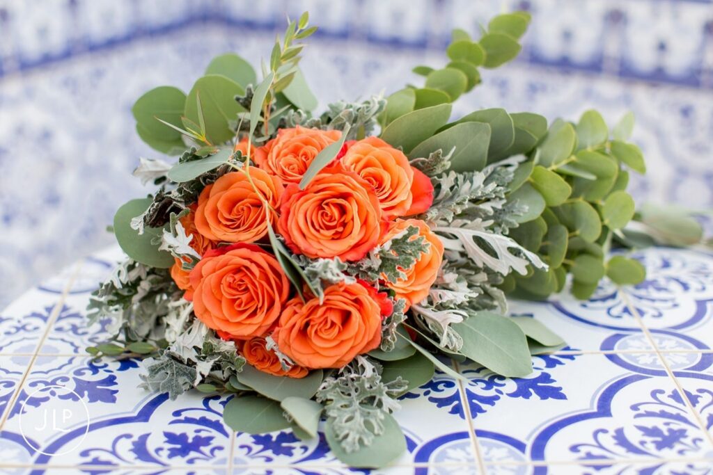 Close-up of a bridal bouquet with orange roses on blue Portuguese tiles, an Algarve wedding photography detail.