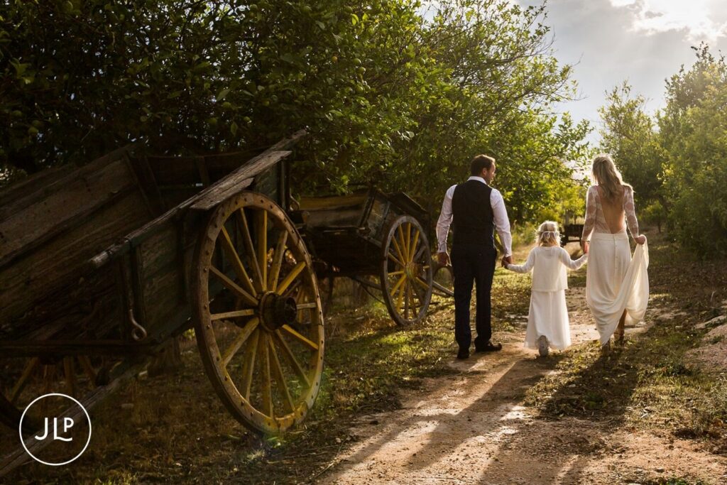Ali and Matty walking through Quinta dos Vales vineyards with a young flower girl at golden hour.