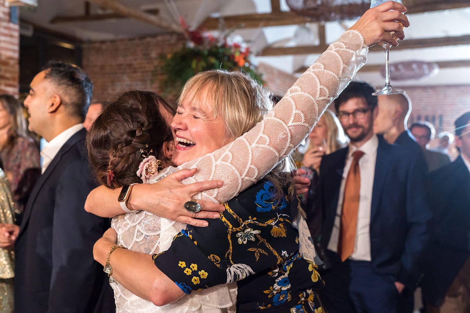 Bride laughing while hugging a wedding guest during an indoor autumn reception at a Berkshire venue.