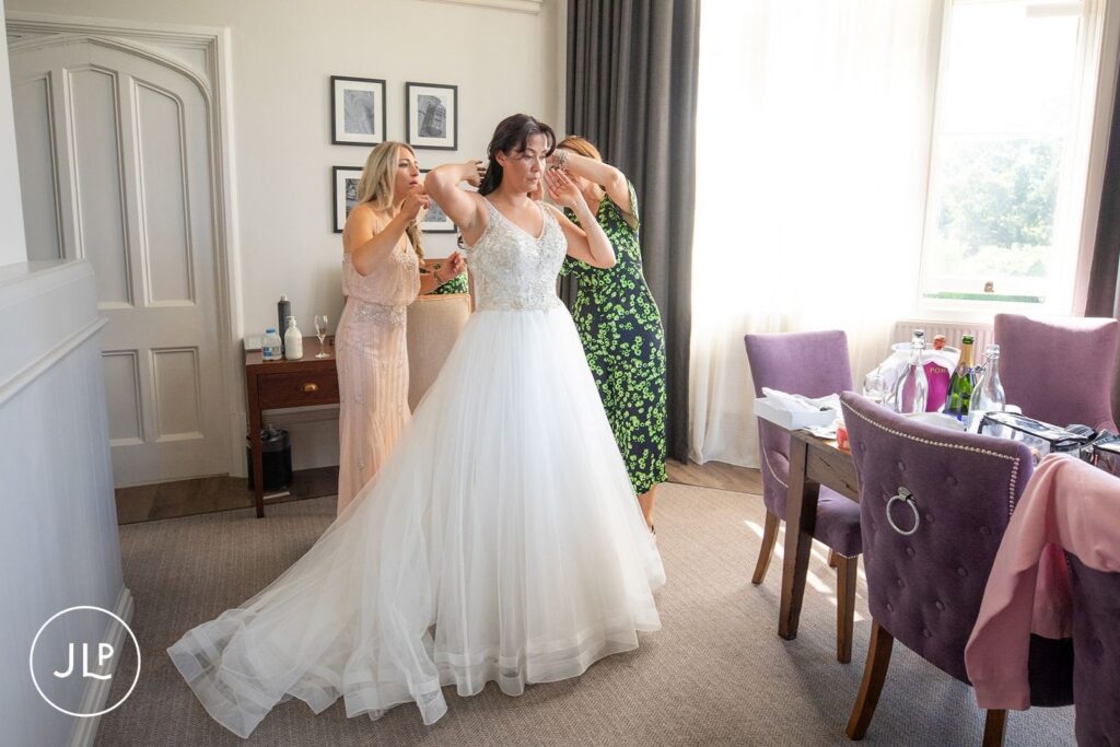 Two bridesmaids help the bride into her beaded gown, capturing a moment of natural wedding photography.