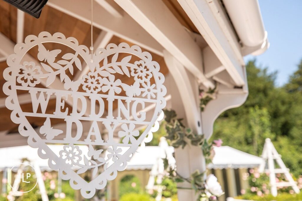 A white laser-cut wooden heart hanging in a gazebo with the words "Wedding Day" for an outdoor ceremony.