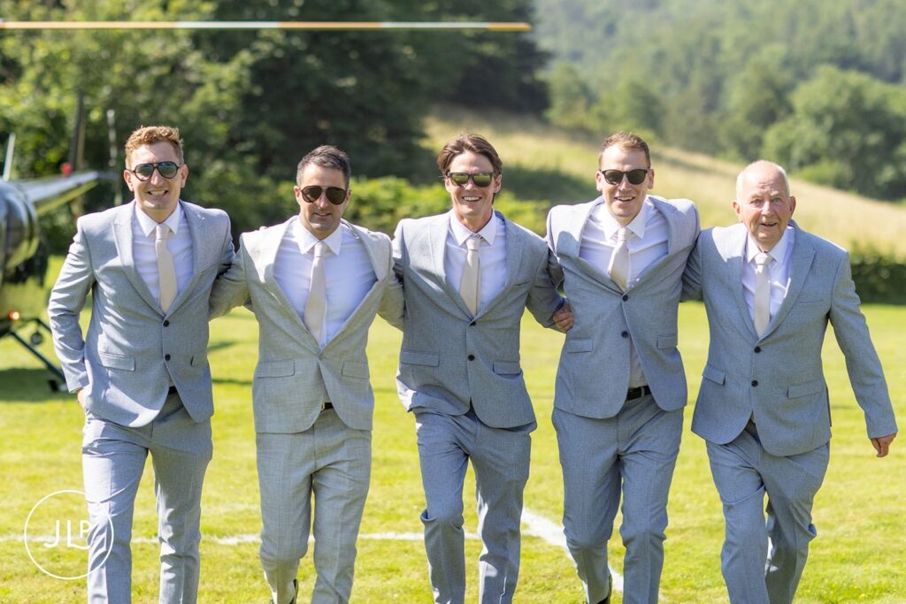 The groom in a light grey suit and sunglasses stands with his groomsmen at a luxury Gloucestershire wedding.