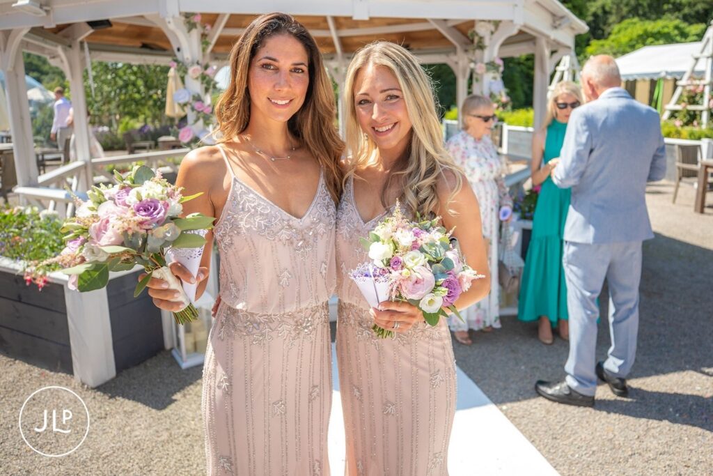 Two bridesmaids in matching beaded blush gowns hold bouquets while posing together at a luxury Gloucestershire wedding venue.