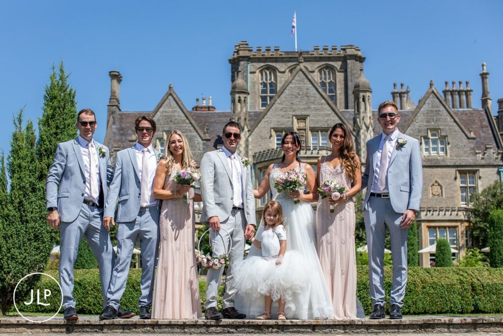 A formal portrait of the bride, groom, bridesmaids, and groomsmen posed in front of the historic De Vere Tortworth Court.